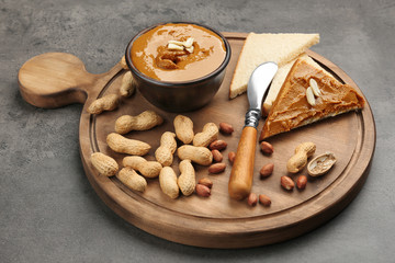 Wooden board with delicious peanut butter, toasts and nuts on table