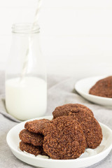 Chocolate coconut cookies on white plate with a glass of milk, vertical.