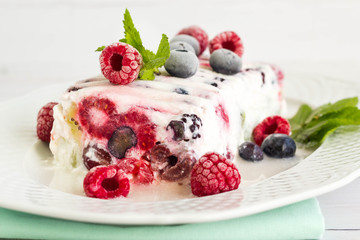 Yogurt cake with colorful fruits and mint leaves served on white plate.