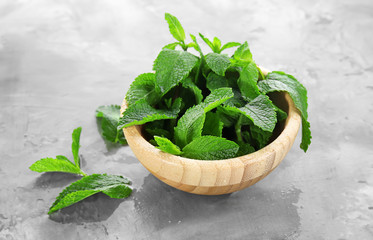 Wooden bowl with fresh mint on grey background