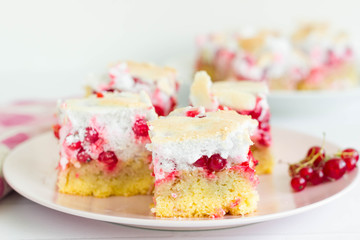 Sponge cake with red currant layer and meringue on top, served on pink plate. 
