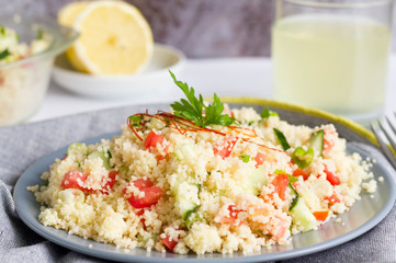 Couscous salad with fresh vegetables served on grey plate on kitchen table.