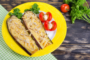 Baked eggplants with parmesan, sunflower seeds and tomatoes. In a yellow dish on a wooden rustic background. A branch of parsley is near.