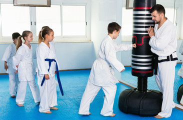Children training karate kicks on punching bag during karate class