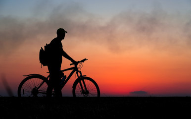 Silhouette of cyclist on the background of red sunset. Biker with bicycle on the field during sunrise