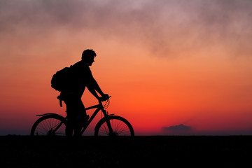 Fototapeta na wymiar Silhouette of cyclist on the background of red sunset. Biker with bicycle on the field during sunrise