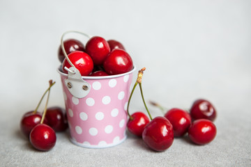 Red cherries in little pink bucket on gray background