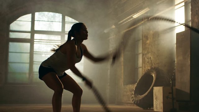 Strong Athletic Woman Exercises with Battle Ropes as Part of Her Cross Fitness Gym Workout Routine. She's Covered in Sweat. Shot on RED EPIC-W 8K Helium Cinema Camera.