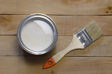 Bank of white paint and brush on a wooden table.