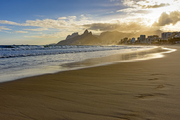 Summer sunset at Ipanema beach in Rio de Janeiro with the light crossing the buildings and hills until arriving at the sea