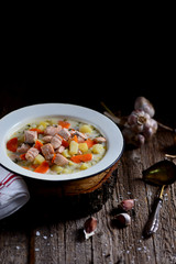 Finnish cream soup with salmon, potatoes and carrots in an old vintage plate on a wooden background. Rustic food, rustic style.