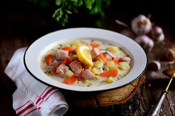 Finnish cream soup with salmon, potatoes and carrots in an old vintage plate on a wooden background. Rustic food, rustic style.