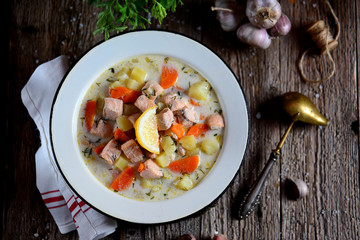 Finnish cream soup with salmon, potatoes and carrots in an old vintage plate on a wooden background. Rustic food, rustic style.