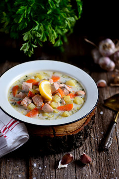 Finnish cream soup with salmon, potatoes and carrots in an old vintage plate on a wooden background. Rustic food, rustic style.
