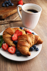 Delicious breakfast with fresh croissants, coffee and ripe berries on old wooden background