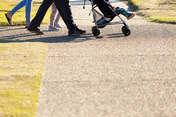  A below waist shot of a family of four, including a baby in a pram, walking and exercising on a...