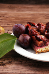 rustic plum cake on wooden background with plums around