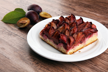 rustic plum cake on wooden background with plums around