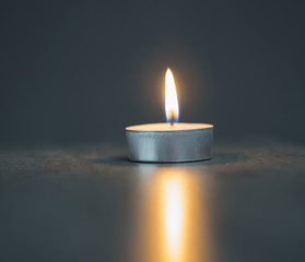 single tea light candle on the soft blurred grey background - obrazy, fototapety, plakaty