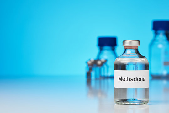 A ampoule of methadone against a blue background. Other laboratory bottles can be seen in the background. (English lettering) in transverse format and space for text