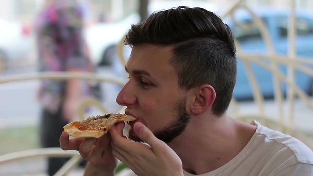 Young man eating pizza in a cafe on the street