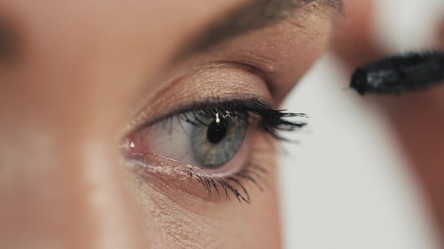 Woman applying mascara on her long eyelashes close up