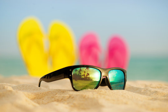 Glasses with yellow and pink sandals stand in the sand against the background of the sea