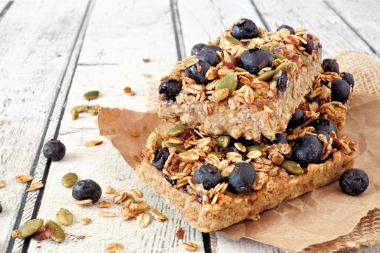 Two stacked superfood breakfast bars with oats and blueberries, side view on rustic white wood