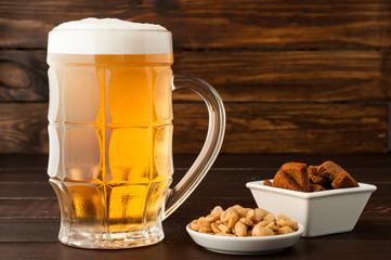 glass of cold frothy lager beer and peanuts plate on wooden table