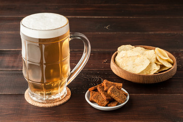 glass of cold frothy lager beer and potato chips plate on wooden table
