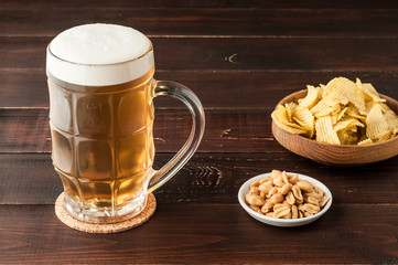 glass of cold frothy lager beer and potato chips plate on wooden table