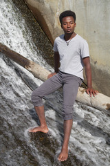 young man barefoot in river sitting on tree trunk waterfalls