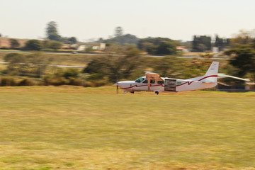 Fototapeta premium Small white airplane taking off. Grams and trees. Panning efect photo. Speed airplane taking off in dirt track. Skydive dropzone.