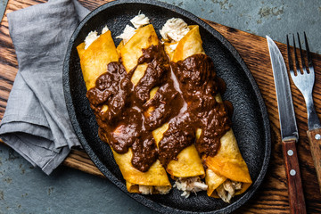 Mexican cuisine. Traditional Mexican chicken enchiladas with spicy chocolate salsa mole poblano. Enchiladas with sauce moole from Puebla, Mexico - obrazy, fototapety, plakaty