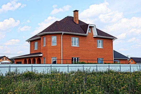 Современный коричневый кирпичный дом за забором в траве