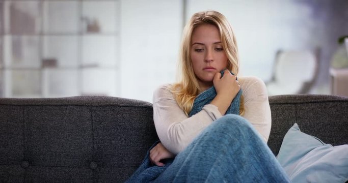Sad young woman sitting on the couch holding a blanket