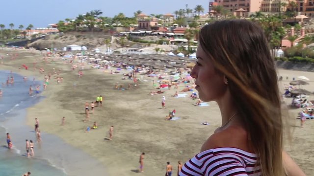 Tenerife. Spain. Beautiful blond girl on vacation observes Del Duque beach (Playa del Duque) located in Costa Adeje in South of Tenerife island in Las Americas..