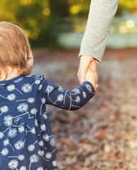 Toddler girl holding hands with her mother outside on a fall day