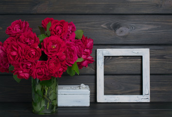Roses in vase and and vintage photo frame on background of wooden planks in rustic style