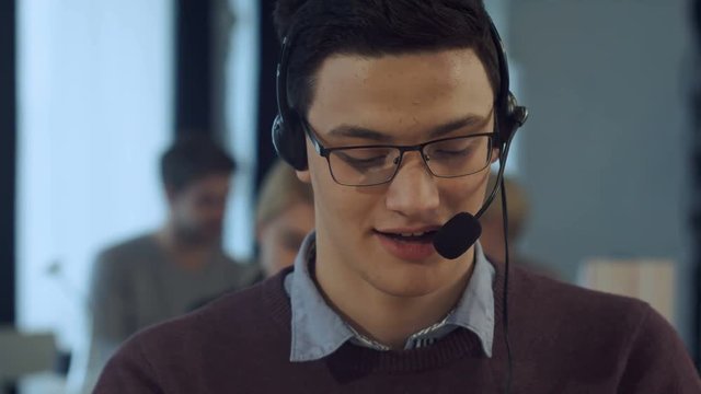 Young man working at a computer in a call centre smiling