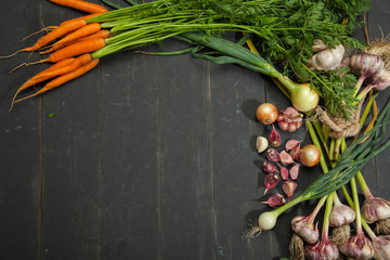 Fresh garlic, carrots and onions and vegetables on black wooden background