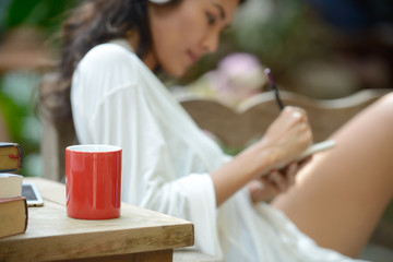Red coffee cup and, Blur background beautiful young woman take a note in a garden