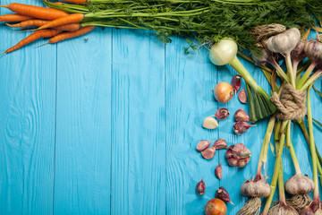 Fresh carrots, garlic and onions on a blue background