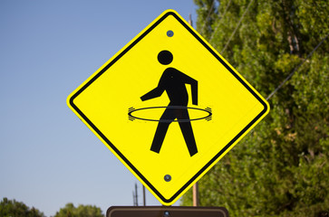 A bright yellow pedestrian crosswalk sign with a hula hoop drawn onto it.