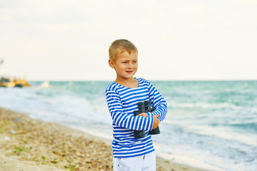 A boy walks on the beach with binoculars
