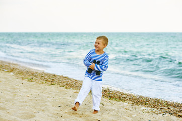 A boy walks on the beach with binoculars
