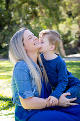 Fototapeta premium Young son kissing Mother on cheek whilst sitting outdoors in park