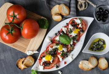 Fresh refreshing salad of mozzarella and red tomatoes on white plate. Spilled with olive oil with pieces of black olives, basil and red onions