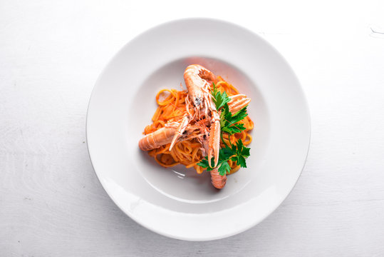 Pasta and tiger shrimp in tomato sauce. Italian traditional food. On a wooden background. Top view. Free space for your text.