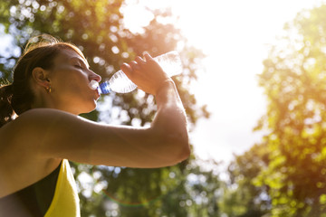 Young beautiful brunette drinking water from a bottle after running workout - obrazy, fototapety, plakaty